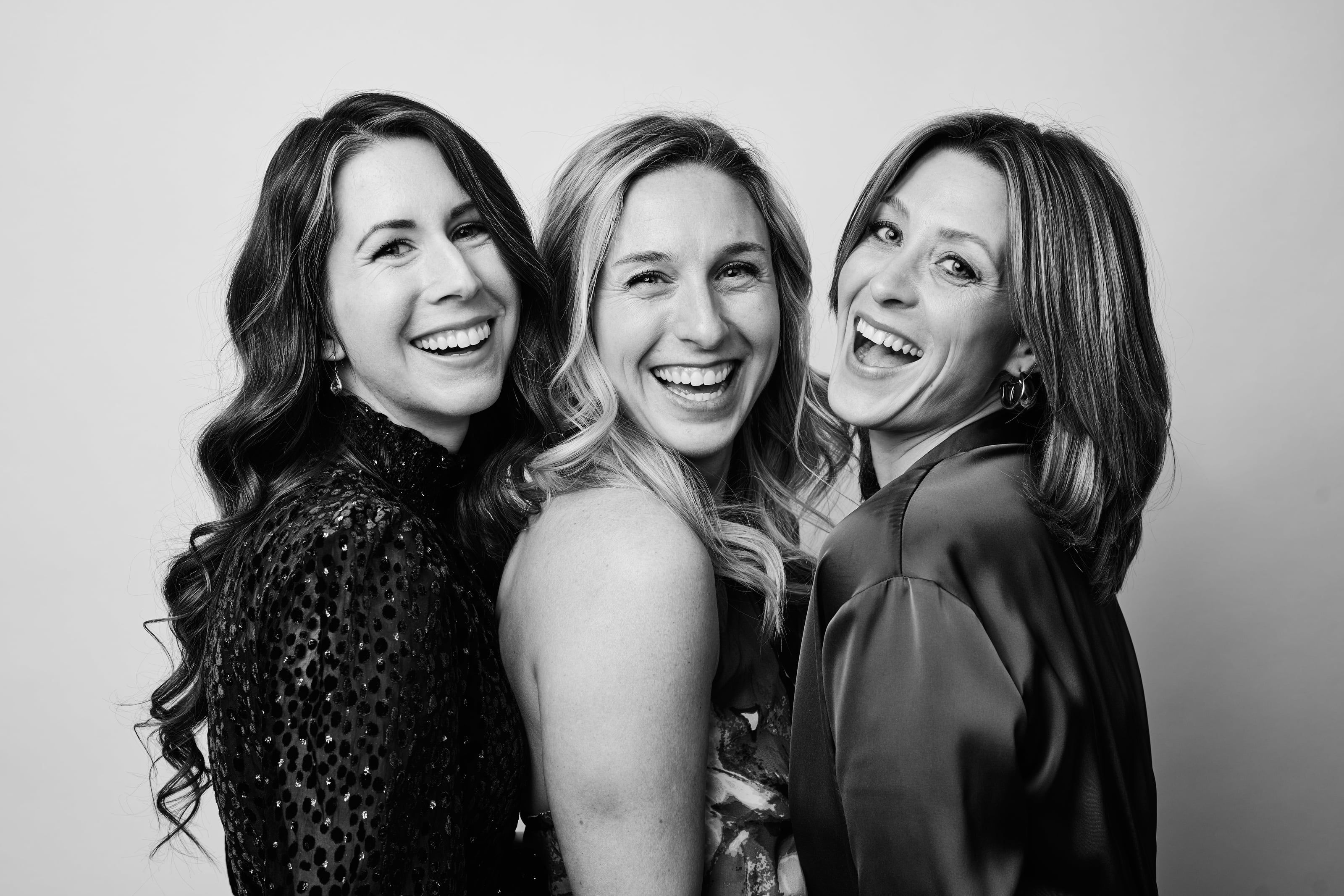 Three women in editorial evening wear share a candid laugh — a black-and-white gala portrait by Studio JK.